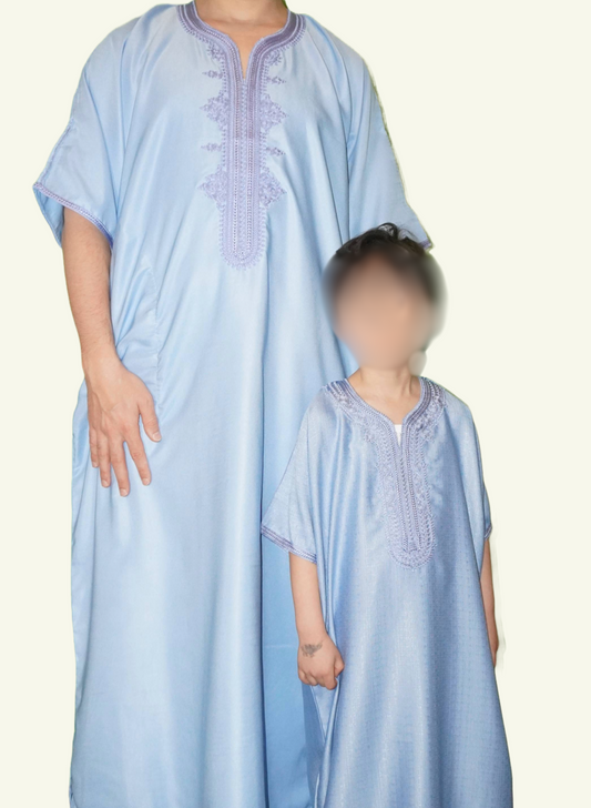 Ein stilvolles Bild, auf dem eine Djellaba Noble in Babyblau gezeigt wird, ein Symbol für Eleganz und Tradition. Das Strickmuster auf der Brust und die Enden der Ärmel sind mit babyblauen Strick verziert, während ein Erwachsener und ein Kind im Partner-Look dieses Kleidungsstück tragen.