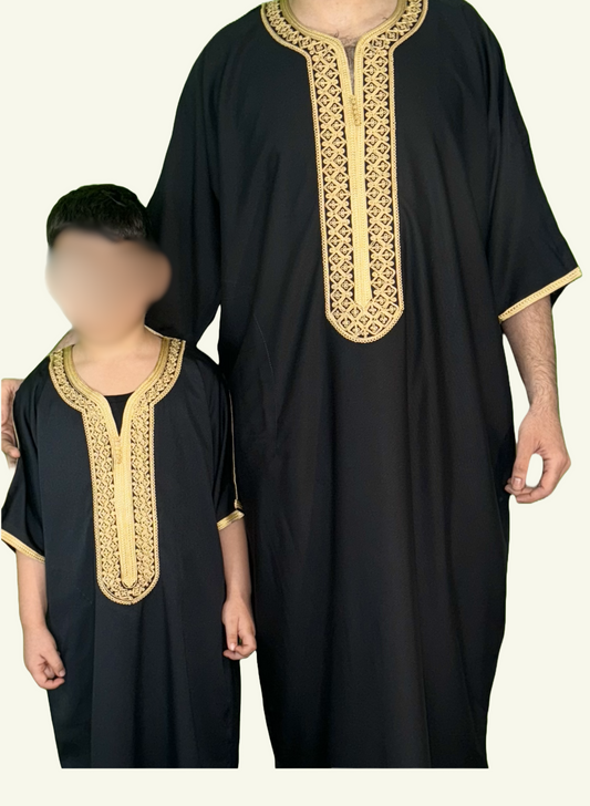 Ein stilvolles Bild, auf dem eine Djellaba Noble in Schwarz gezeigt wird, ein Symbol für Eleganz und Tradition. Das Strickmuster auf der Brust und die Enden der Ärmel sind mit goldenem Strick verziert, während ein Erwachsener und ein Kind im Partner-Look dieses Kleidungsstück tragen.