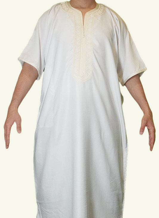 Ein stilvoller Körper, auf dem eine Djellaba Noble in weiß liegt, ein Symbol für Eleganz und Tradition. Das Strickmuster auf der Brust und die Enden der Ärmel sind mit weißem Strick verziert.